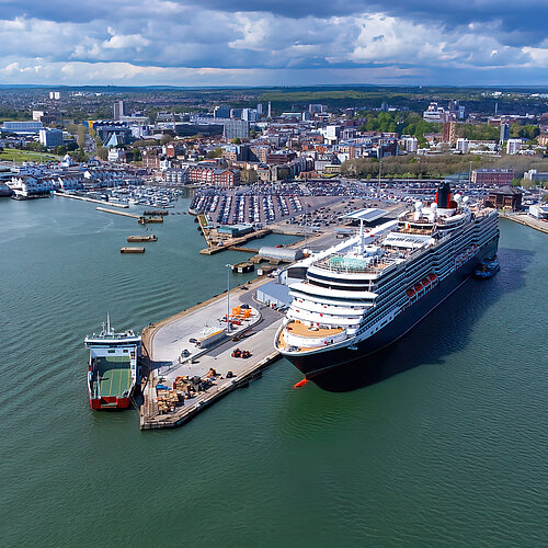 Kreuzfahrtschiff und Fähre am Hafen von Southampton, Stadt im Hintergrund unter bewölktem Himmel.